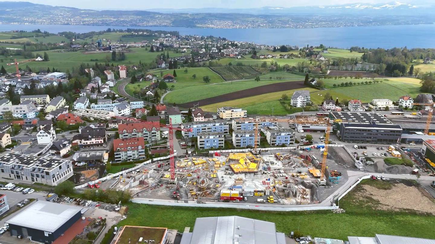 Drohnenflug über aktive Mehrfamilienhaus-Baustelle am Schweizer See mit Kranen und Bauleitercontainer.